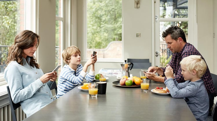A family sitting around a dinner table while using their phones